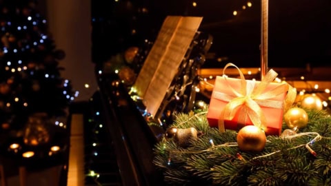 Weihnachtsgeschenk mit goldener Schleife auf einem Klavier mit Noten, Geschenkideen für Sängerinnen, Sänger, Chor und Musiker