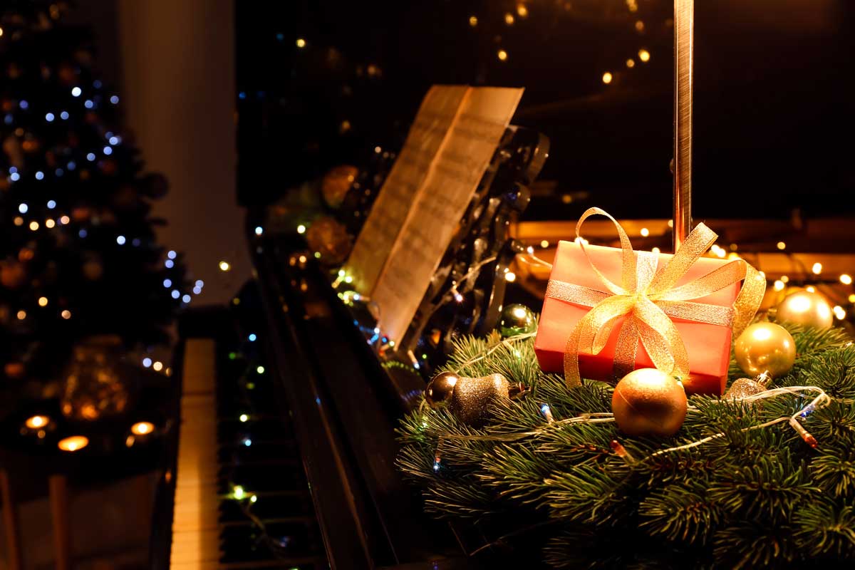 Weihnachtsgeschenk mit goldener Schleife auf einem Klavier mit Noten, Geschenkideen für Sängerinnen, Sänger, Chor und Musiker