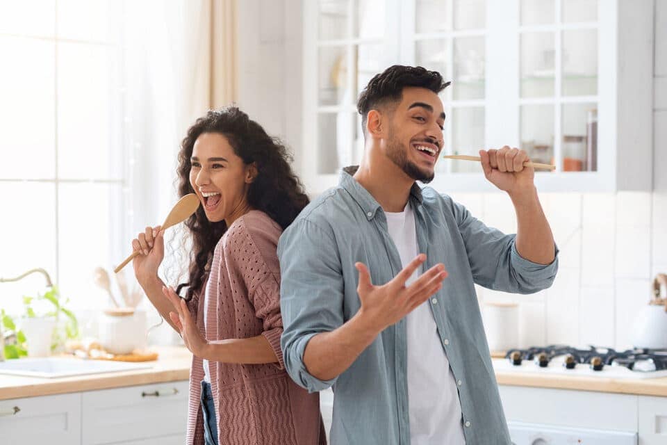 Ein junges Pärchen singt in der Küche: Singen lernen online macht Spaß, zum Beispiel mit der Gesangs App